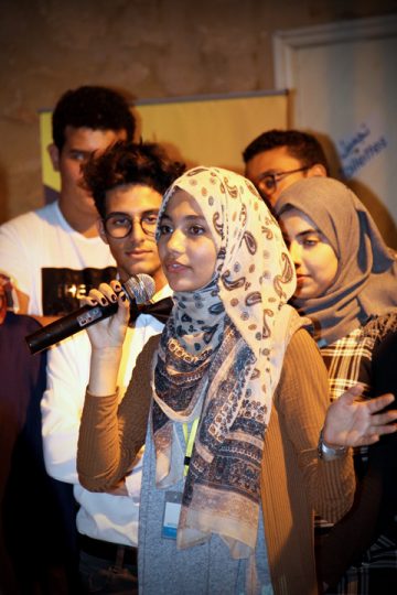 A female Mosta9bali participant speaking at an event in front of other participants